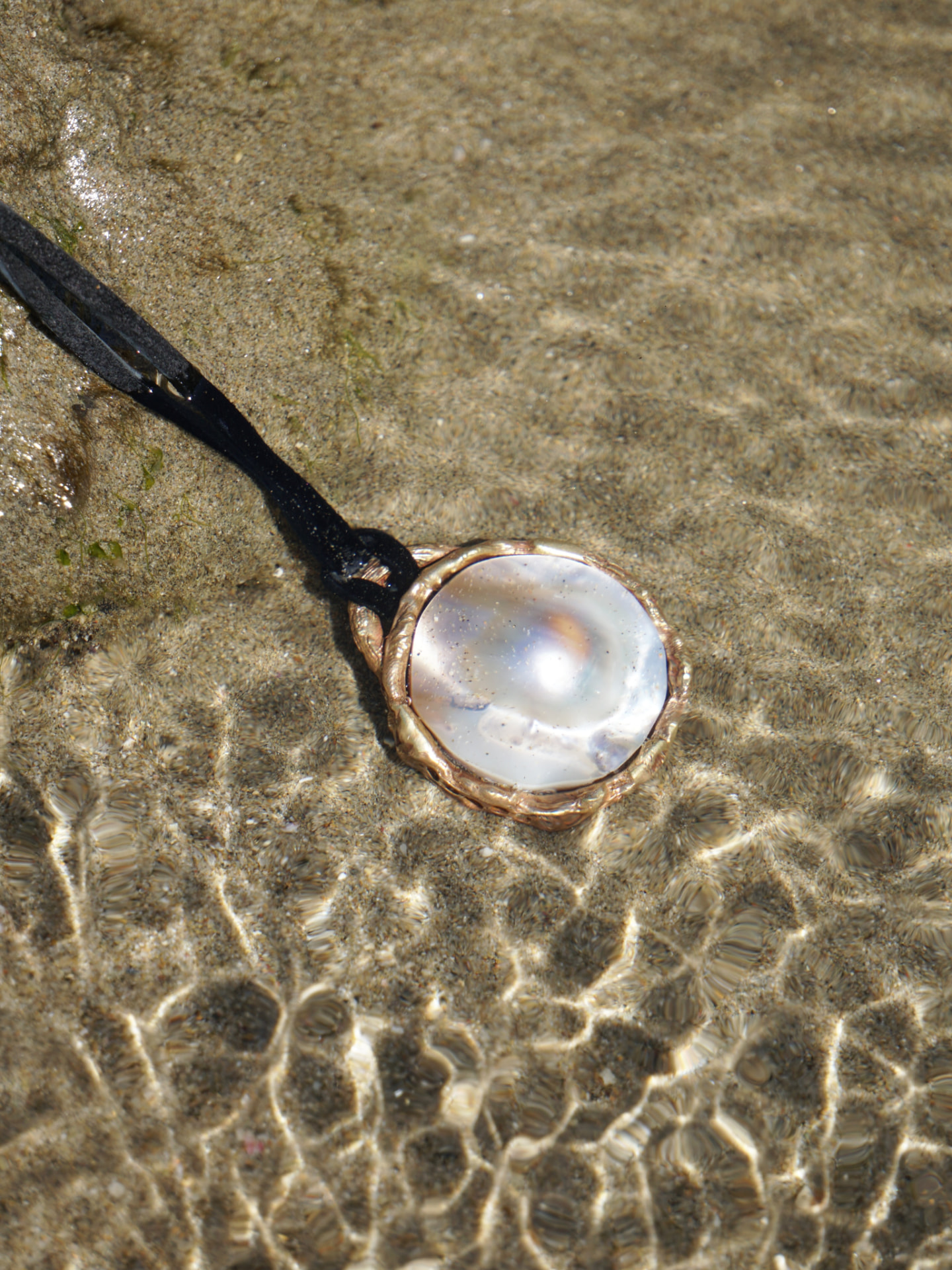 Colgante bajo el agua: perla, arena y luz natural.
